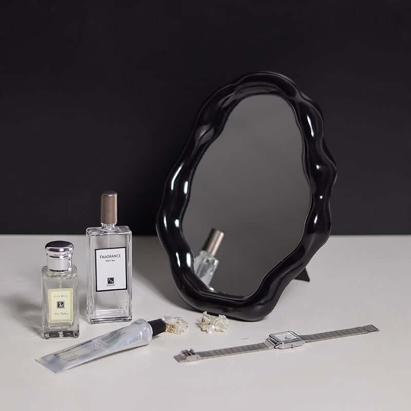 Nordic cloud-shaped vanity mirror with a black wavy frame on a table alongside perfumes, jewelry, and a watch.