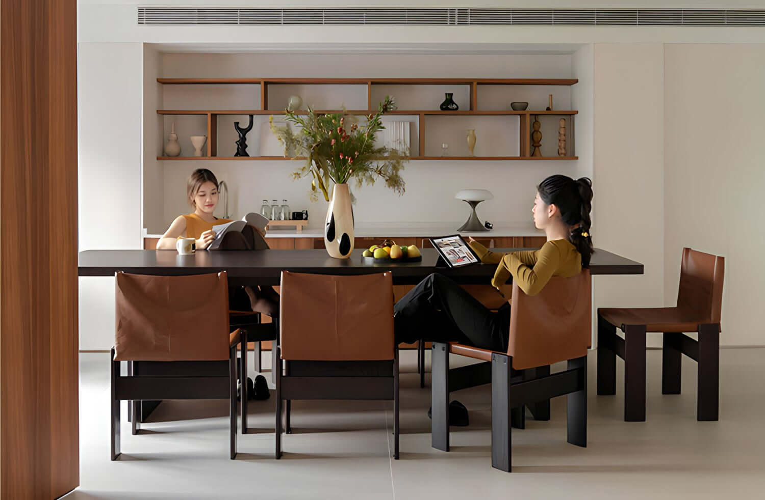 Elegant dining room with Gora dining table, cherry wood, Monk chairs with leather seats, women enjoying cozy ambiance, modern decor.