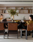 Elegant dining room with Gora dining table, cherry wood, Monk chairs with leather seats, women enjoying cozy ambiance, modern decor.