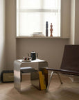 Minimalist stainless steel bedside table with books and a coffee set in a modern room setting.
