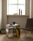Minimalist stainless steel bedside table with books and a coffee set in a modern room setting.