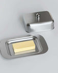 Stainless steel butter dish with lid, featuring a modern design and a stick of butter, by LoveÉcru.
