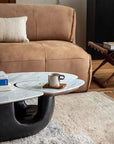 Contemporary Wabi-Sabi coffee table with wood and stone top, smooth curve base, in a modern living room setting with books and mug.