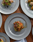 Stainless steel round plates with gourmet dishes on a wooden table, showcasing VINTAGE INOX’s chic design and durability.