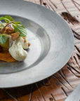 Stainless steel round plate with gourmet dish on a textured wooden table