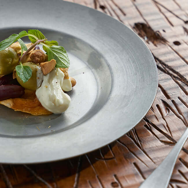 Stainless steel round plate with gourmet dish on a textured wooden table