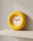 Yellow Bagel Clock resting on a travertine shelf