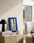 Klein Blue Onda Wave Mirror on a shelf beside a black lamp