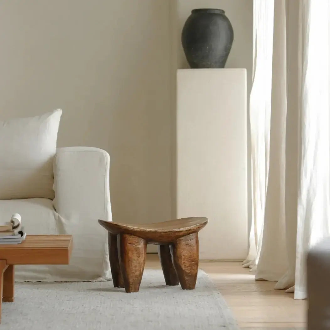 African Senufo wood milk stool with natural textures in a modern living room setting.