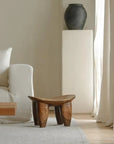 African Senufo wood milk stool with natural textures in a modern living room setting.