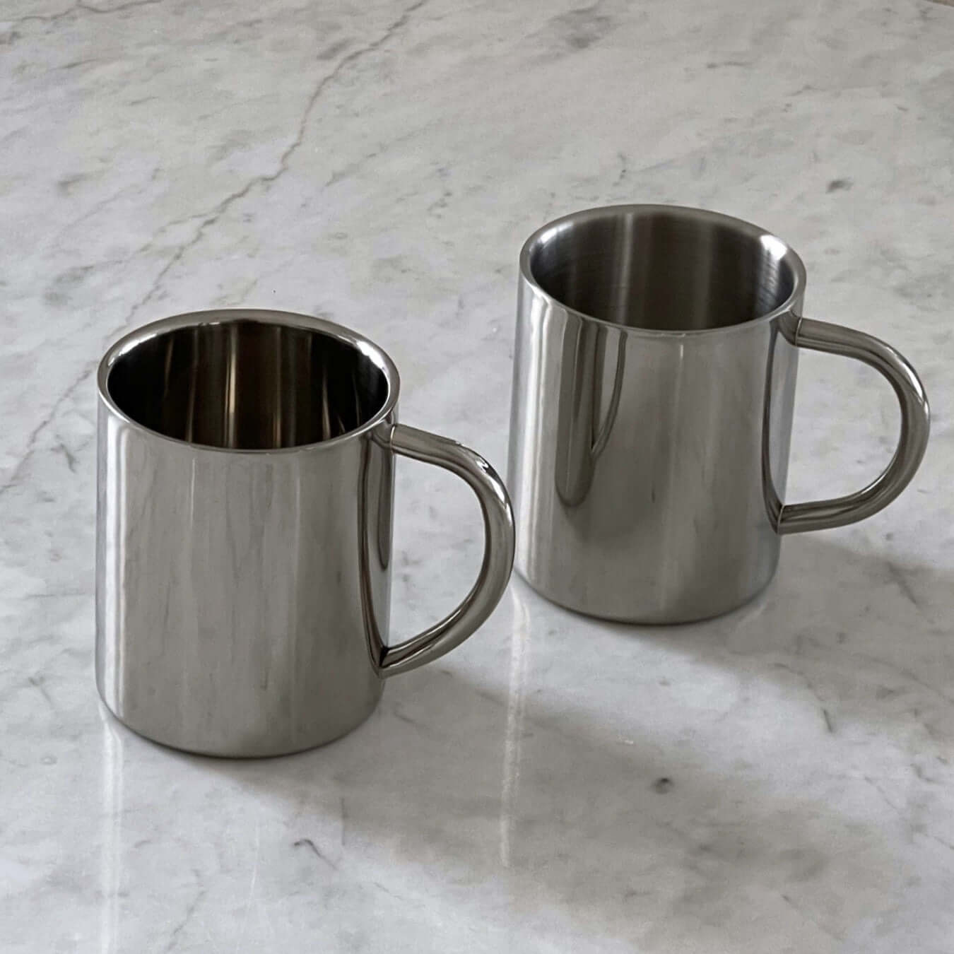 Double-layer glossy stainless steel cups on a marble surface, ideal for keeping beverages at the perfect temperature.
