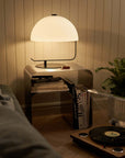 Minimalist stainless steel bedside table with a modern lamp, books, and a cozy living room setting.