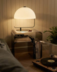 Minimalist stainless steel bedside table with a modern lamp, books, and a cozy living room setting.