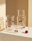 Cherry Glass Pitcher with two cups and a cherry on a stone surface