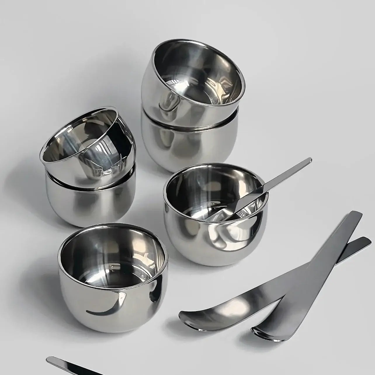 Stainless steel bowls and minimalist dessert spoons set, perfect for modern kitchenware and serving ice cream or coffee.