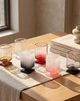 Sculpted Pedestal Glasses in frosted pink, black and clear on a stone ledge