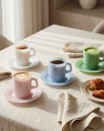 Pastel Muse Mugs in pink, blue and green on a breakfast table with croissants