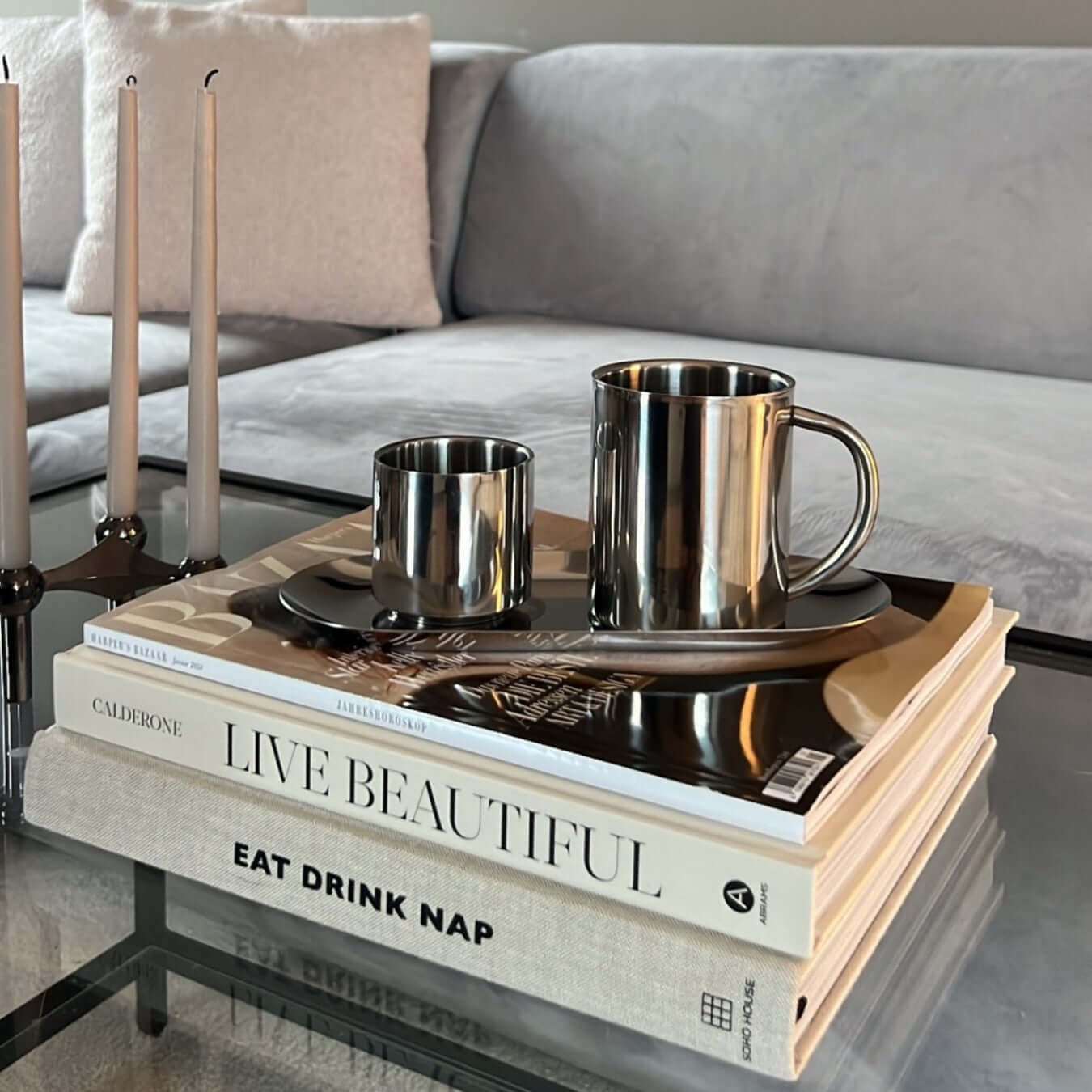 Milano Duo Set stainless steel coffee cups on stack of lifestyle books in modern living room setting.