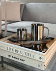 Milano Duo Set stainless steel coffee cups on stack of lifestyle books in modern living room setting.