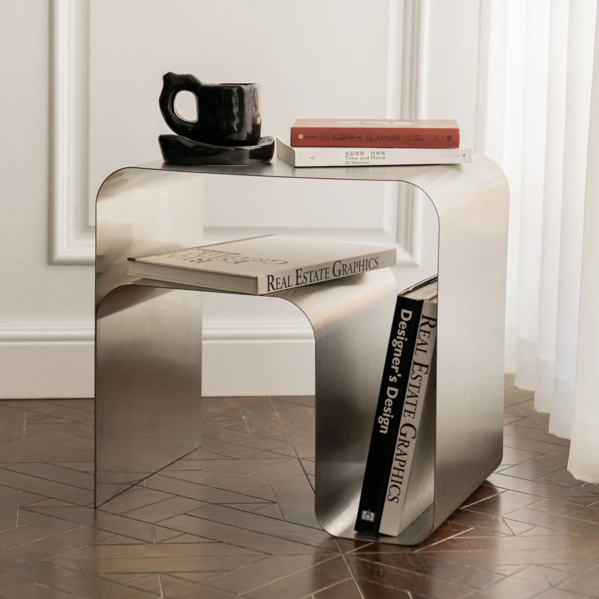 Minimalist stainless steel bedside table with books and mug, featuring modern design, perfect for elegant home decor.