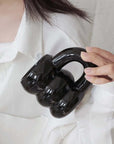 Person holding a black ceramic mug shaped like brass knuckles, wearing a white shirt.