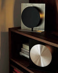 Bauhaus Aura Bedside Lamp lit on a wooden shelf, black disc with glowing halo