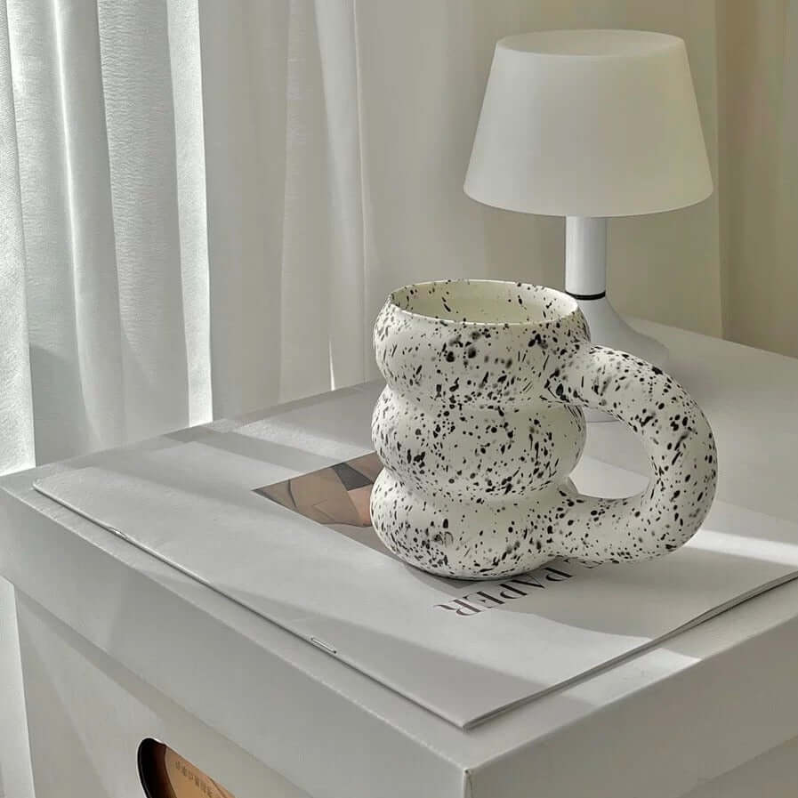 White speckled ceramic mug with a unique design on a table beside a white lamp.