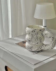 White speckled ceramic mug with a unique design on a table beside a white lamp.