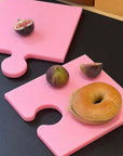 Pink Puzzle Pop Chopping Boards with a bagel and figs on a black counter
