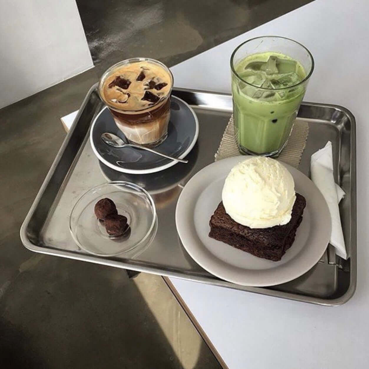 Minimalist stainless steel tray with iced coffee, matcha latte, and dessert at a modern café.