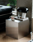 Minimalist Bauhaus Stainless Steel Side Table, a brushed cube beside a leather sofa with a coffee mug