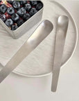 Minimalist dessert spoon set of 2 on a plate with blueberries, ideal for serving modern desserts and coffee, handmade stainless steel.