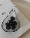 Liora Hand-Blown Glass Scoop Bowl holding black olives on a book