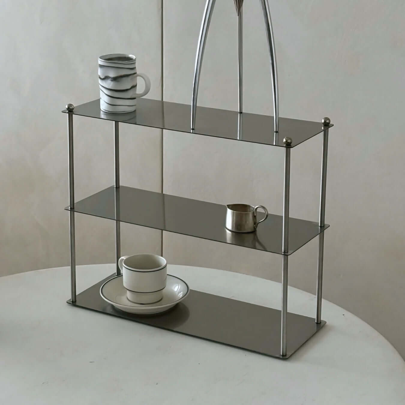 Modern Aira Stainless Shelf with minimalist design holding cups and decor on a smooth tabletop, showcasing sleek elegance.