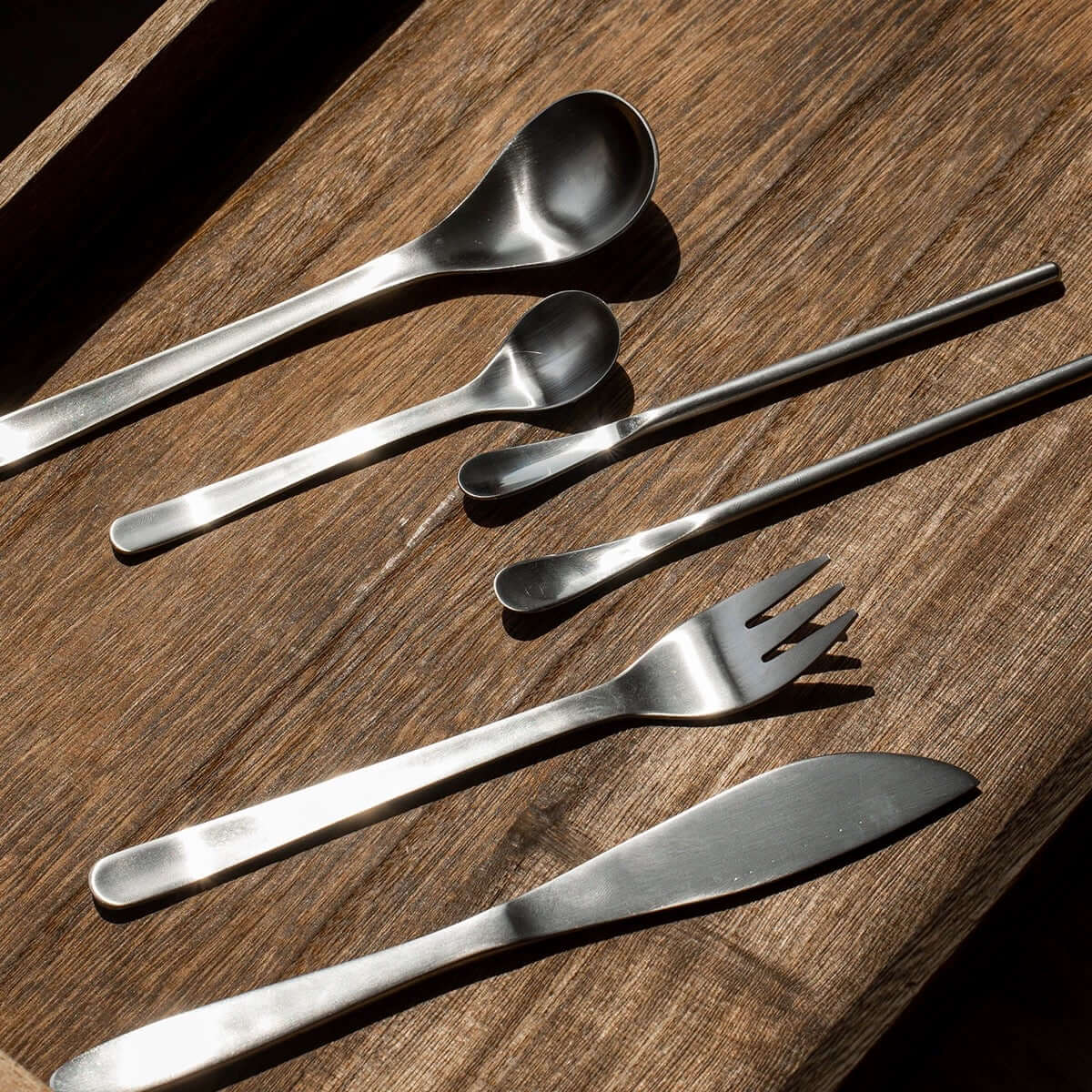 Japanese retro stainless steel cutlery set on wooden surface, featuring spoons, fork, and knife for elegant dining.