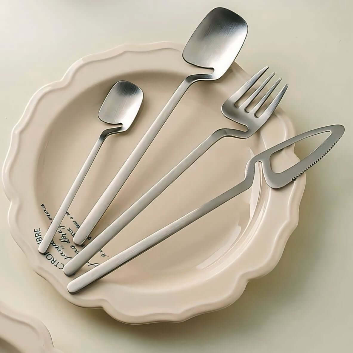 Minimalist stainless steel flatware set on ceramic plate, featuring modern spoons, fork, and knife with Scandinavian-inspired design.
