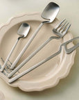 Minimalist stainless steel flatware set on ceramic plate, featuring modern spoons, fork, and knife with Scandinavian-inspired design.