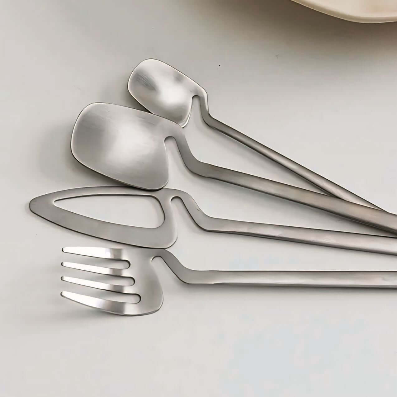 Minimalist stainless steel flatware set with modern Scandinavian design on a white table.