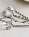 Minimalist stainless steel flatware set with modern Scandinavian design on a white table.