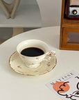 Retro French blossom cup and saucer set with coffee, placed on a white table near a book and wooden shelf.