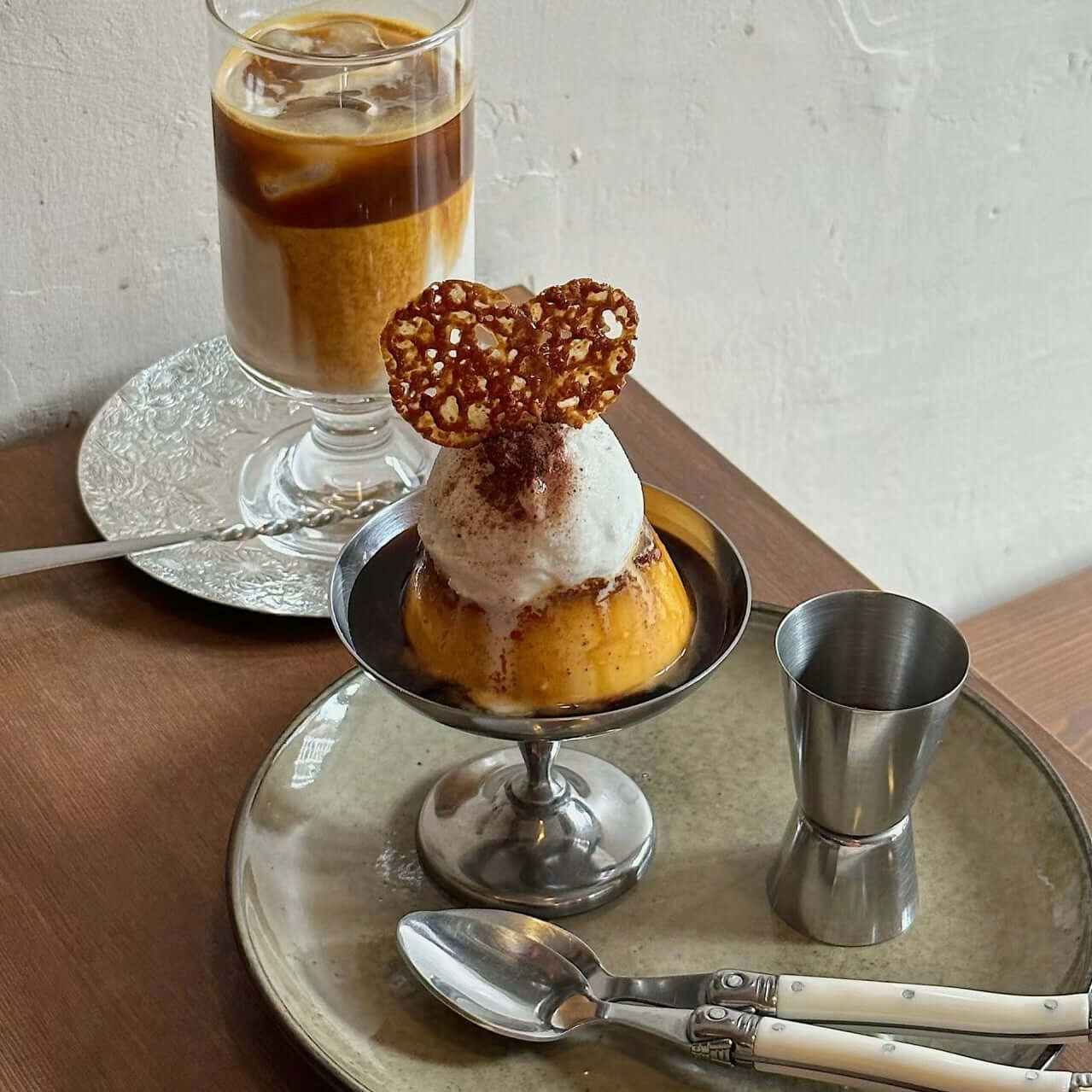 Elegant dessert cup with ice cream and heart-shaped cookie, paired with iced coffee on rustic table setting with stainless steel accents.