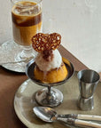Elegant dessert cup with ice cream and heart-shaped cookie, paired with iced coffee on rustic table setting with stainless steel accents.