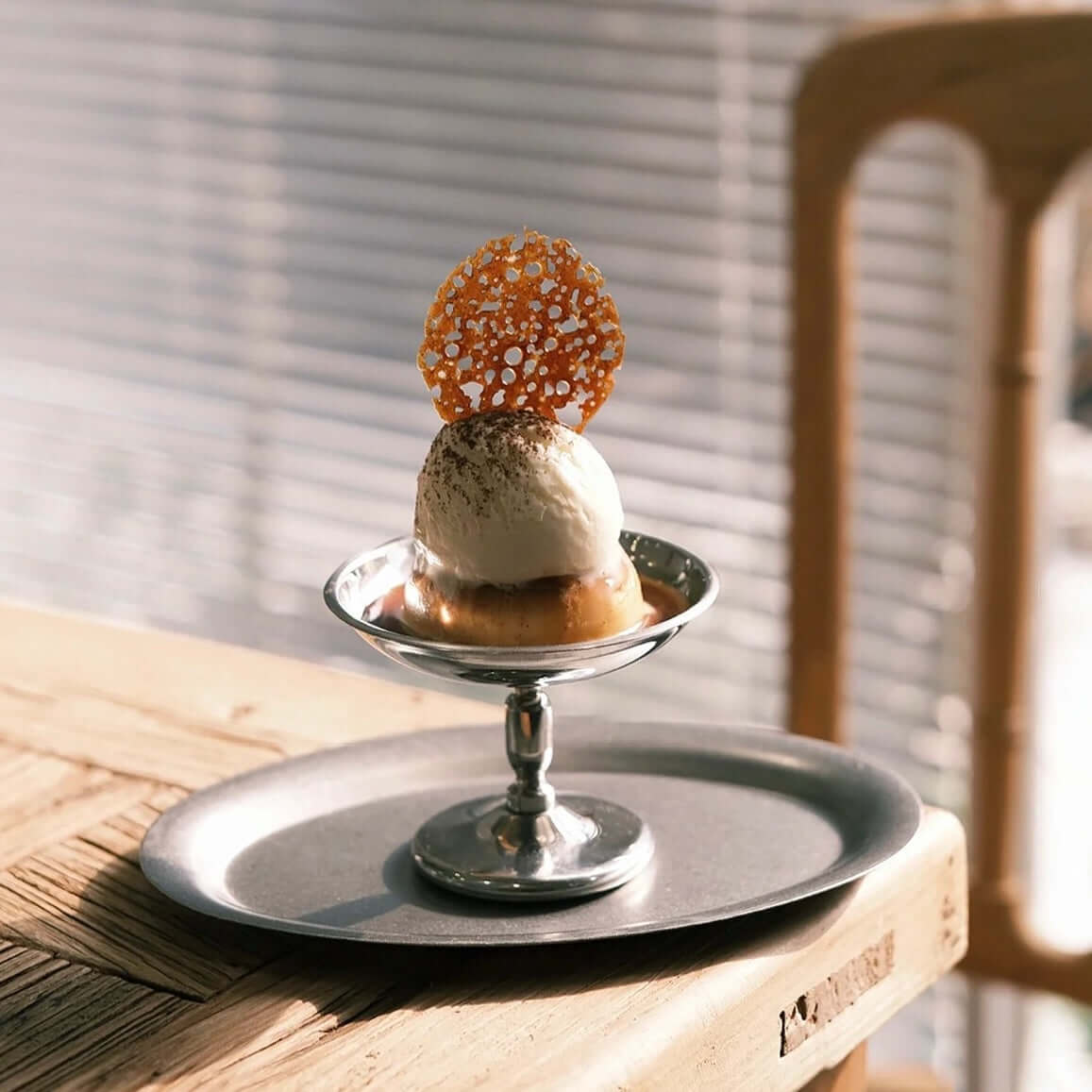 Elegant Dessert Cup with ice cream and caramel garnish on stainless steel dish in a sunlit dining setting.