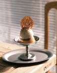 Elegant Dessert Cup with ice cream and caramel garnish on stainless steel dish in a sunlit dining setting.