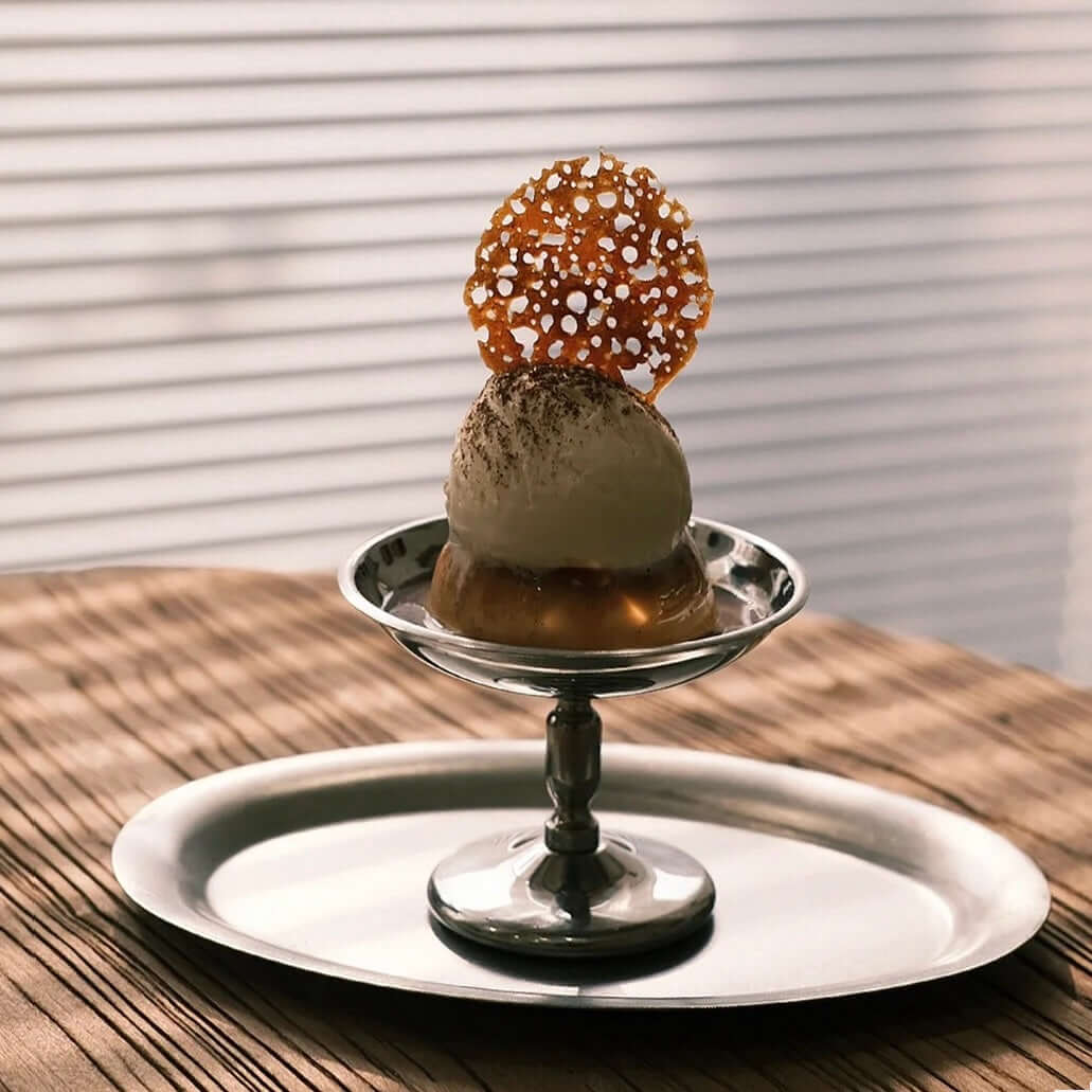 Elegant dessert displayed on a polished stainless steel cup with artistic garnish, set atop a matching tray.