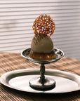 Elegant dessert displayed on a polished stainless steel cup with artistic garnish, set atop a matching tray.