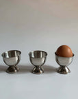 Stainless steel egg holders set with one egg, elegant matte finish, perfect for kitchen decor and brunch settings.