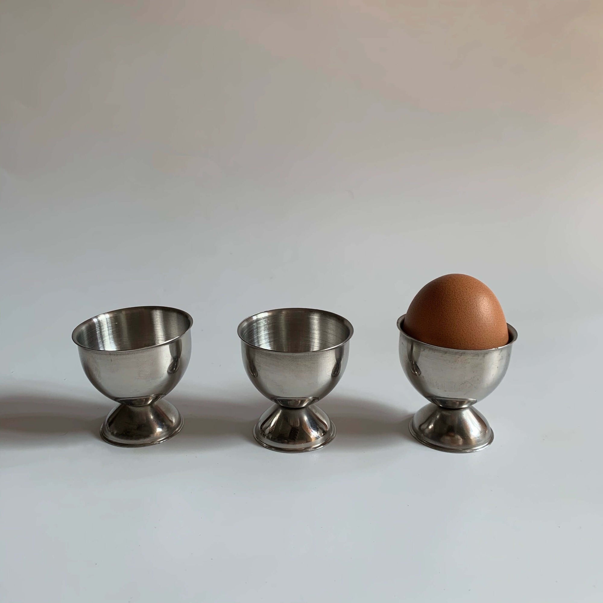 Stainless steel egg holders set with one egg, elegant matte finish, perfect for kitchen decor and brunch settings.
