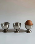 Stainless steel egg holders set with one egg, elegant matte finish, perfect for kitchen decor and brunch settings.