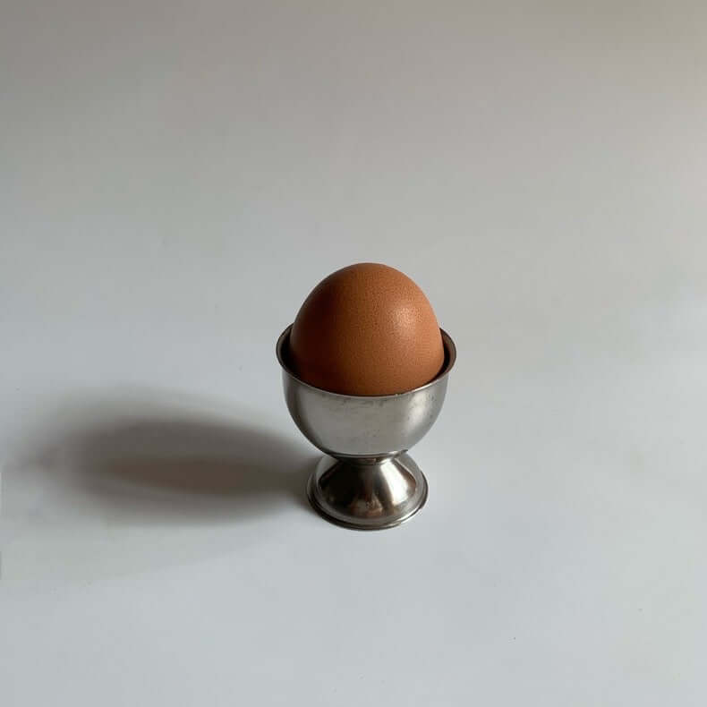 Stainless steel egg holder with a brown egg, featuring an elegant matte finish, perfect for kitchen decor and family breakfasts.